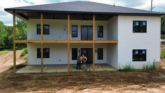 Man, Women and young girl in front of their unfinished home