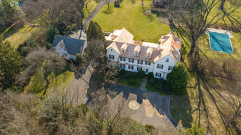 Aerial View of a Cedar Shingle Roof on a Beautiful 1740's Colonial Home, Additionally it includes White Stucco Dormers, Three Copper Flat Seam Roofs, And One Standing Seam Roof. Aerial view of a cedar shingle roof on a beautiful 1740s colonial home. The home has white stucco dormers, three copper flat seam roofs, and one standing seam roof. The roof is in good condition and shows the natural beauty of the cedar shingles. The home is surrounded by trees and shrubbery, giving it a rustic feel.