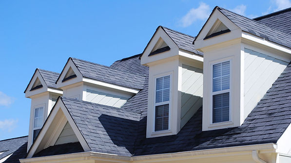Image of a newly constructed house with a grey shingle roof, four dormers, and light grey siding with white trim. The roof is sloped and has a variety of pitches. The grey shingles are a classic choice that complement the light grey siding. The dormers add additional space and light to the house. The white trim provides a touch of contrast and highlights the details of the house. The overall effect is a beautiful and modern home that is sure to turn heads.