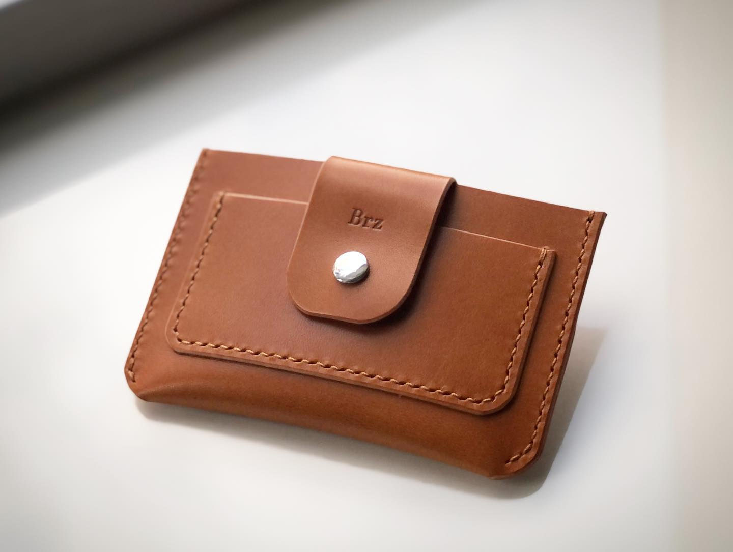 A tan leather wallet with a front snap pocket, contrast stitching
