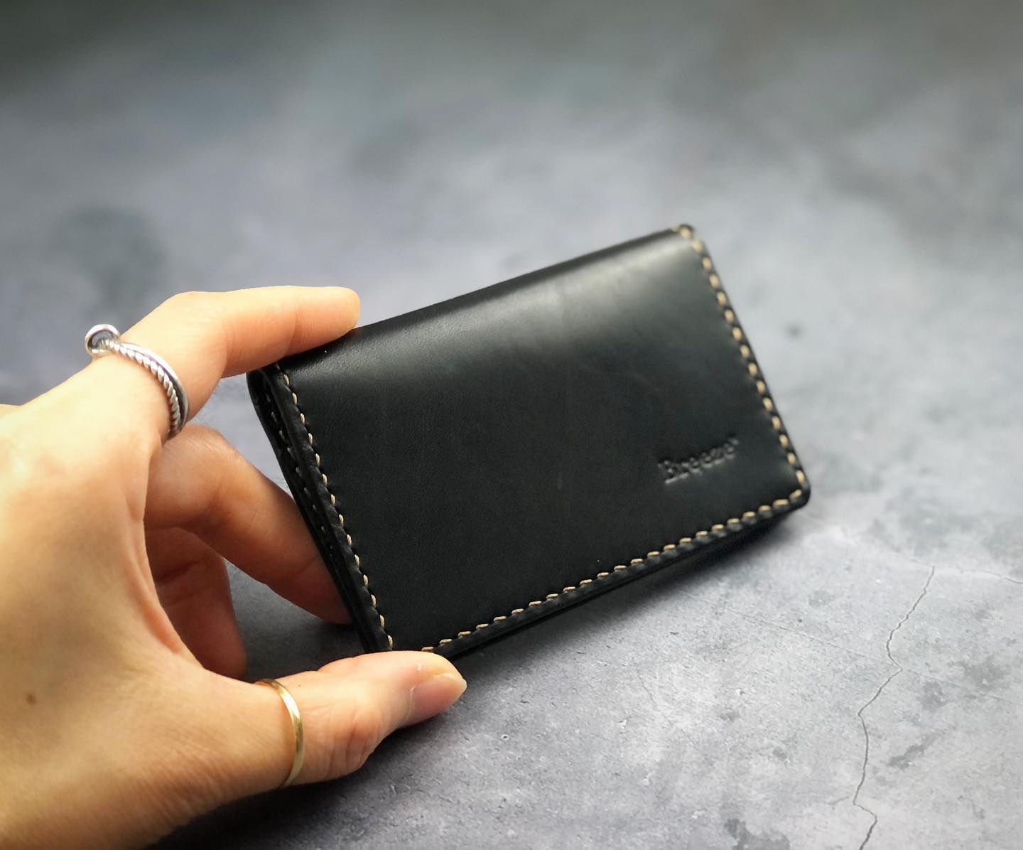 A hand holding a black leather wallet with white contrast stitching, the brand name 'Breeze' subtly imprinted