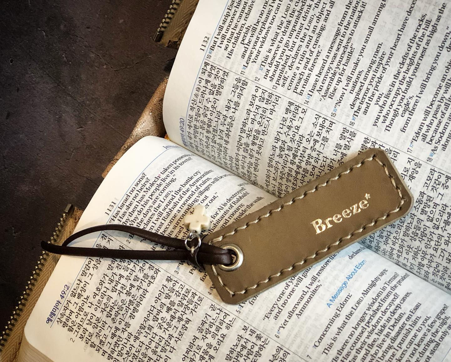 A hand-made tan leather bookmark with "Breeze*" embossed on it, resting on an open book with Asian script, adorned with a bro