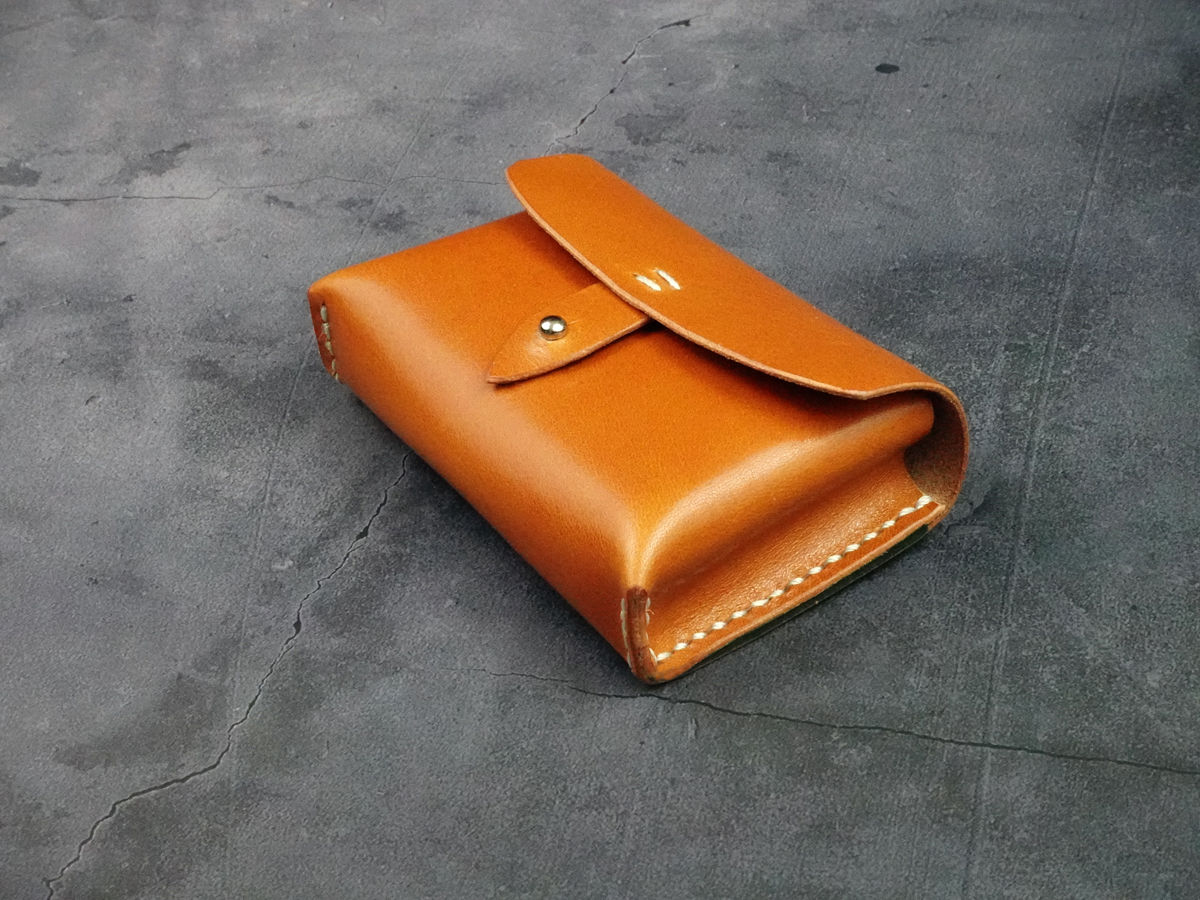 Burnt orange leather wallet with snap closure on a dark grey textured surface