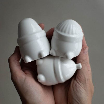 Drei kleine, weisse Keramikweihnachtsmänner in zwei Händen. Eine Weihnachtsdekoration.