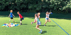 Children playing a game on green grass with blue line, excited faces visible.