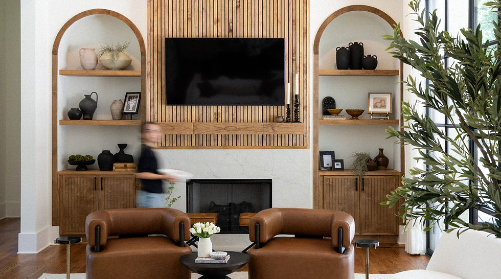 A warm modern living room with wood shelves, TV over fireplace, brown chairs, and a large plant.