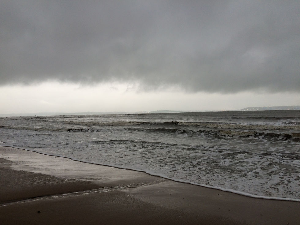 Cloudy sky over a calm beach with gentle waves. The horizon is faintly visible under dark, moody clouds. No text present.