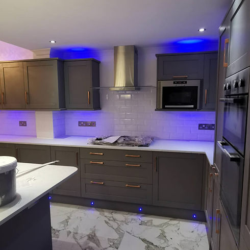 Modern kitchen with grey cabinets, white counters, and blue LED lighting