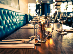 booth seating on one side of a wooden table set with wine glasses and silverwear