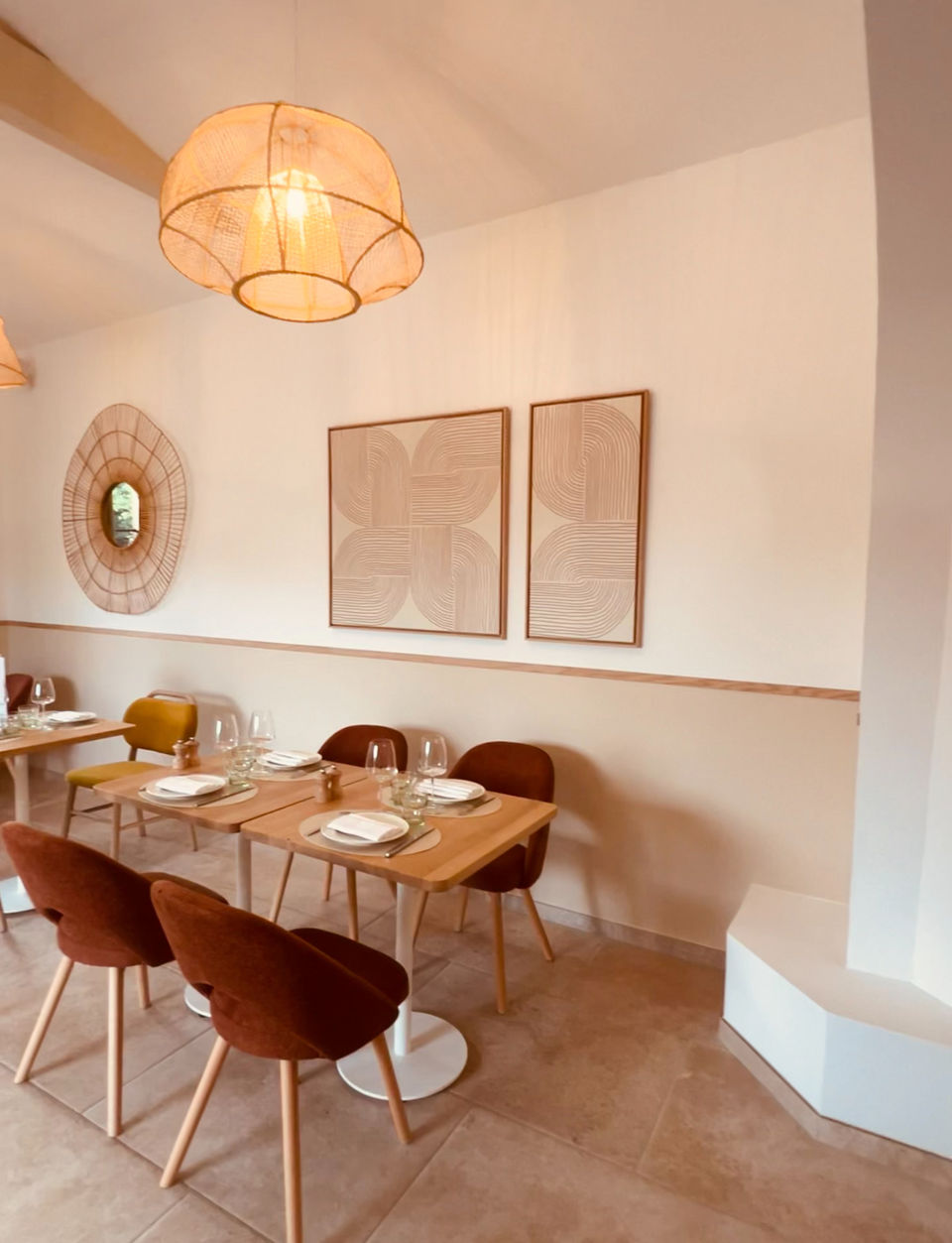 Salle de restaurant avec mobilier en bois, chaises en velours brun, suspensions en fibres naturelles et décoration murale aux motifs graphiques.


