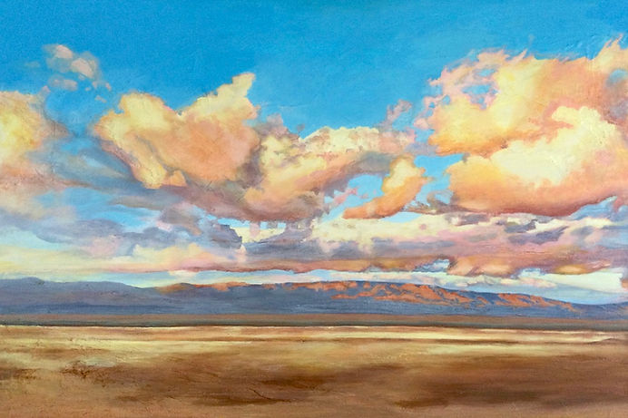 Big golden clouds over and opened desert beneath a bright blue sky, distant mountains