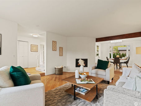 Edmonds Real Estate: Bright living room with beige sofas, green pillows, a wooden coffee table, and a fireplace. Dining table and chandelier in the background.