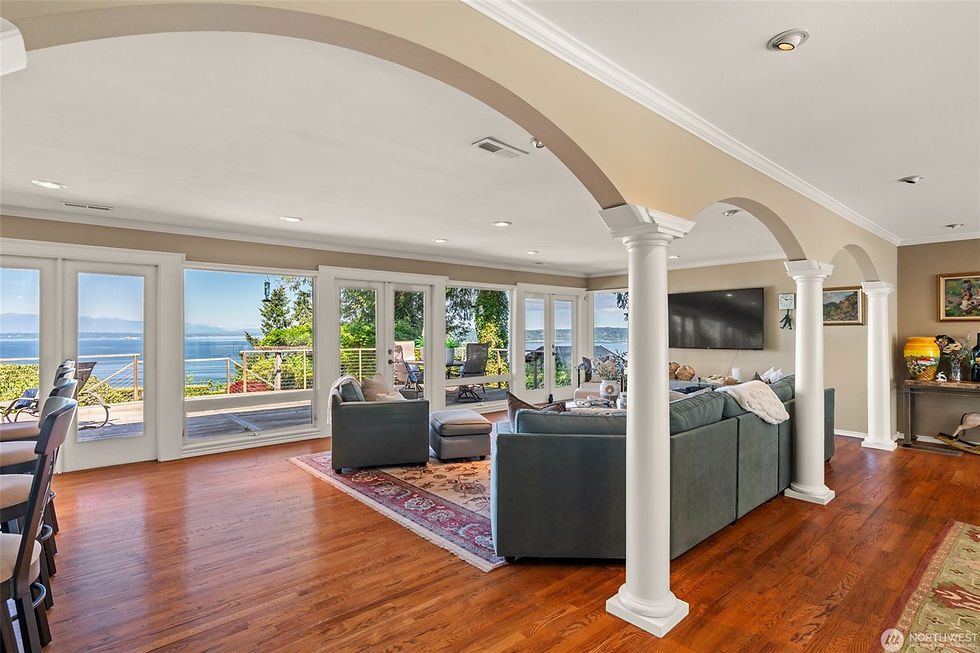 Bright living room with teal sectional, white columns, hardwood floors, and large windows opening to a sunny waterfront view