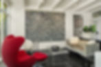 Midcentury modern living room with a large black-and-white textured art piece. Features a red chair, glass coffee table, and velvet sofa with fluffy pillows.