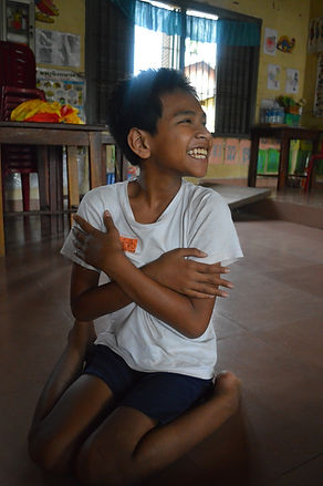 Image of young boy with disabilities sitting on the floor with arms folded smiling_edited.