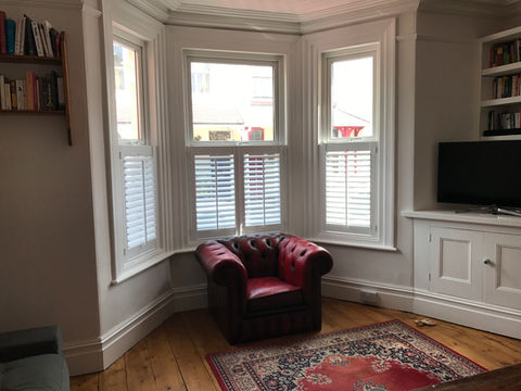 red armchair with a bay window in the background that has new shutters