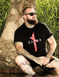 Kunde mit Tattoos trägt Wikinger-Shirt am Wasserufer