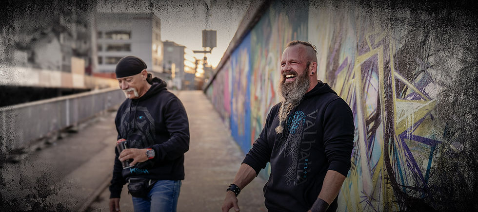 Zwei Männer in North Legendary Hoodies mit Wikinger-Print stehen vor einer Graffiti-Wand in Deutschland und lachen gemeinsam.