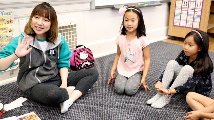 Chinese language teacher waves in the classroom while students look on.