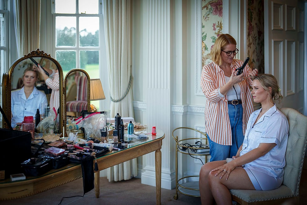 Jennifer Fogerty hair and makeup curling the hair of a bride in the dressing room at Hedsor house. The brides refection in the mirror