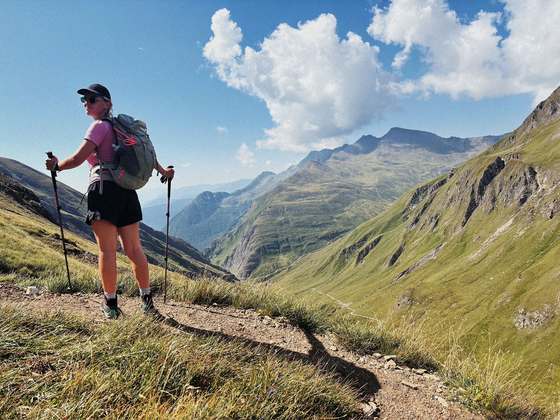Hiker with backpack, hat, and hiking poles standing on a mountain and gazing into the distance—perfect gear for a day trip, inspired by the ultimate packing list for hiking in the mountains.
