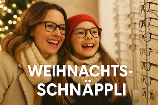 Eine lachende Mutter mit schulterlangem braunem Haar und ihre Tochter mit roter Mütze und Brille stehen nebeneinander vor einem Brillenregal. Beide tragen helle Wollschals und wirken fröhlich und begeistert. Im Hintergrund leuchtet ein Weihnachtsbaum. Unten im Bild steht in weisser Schrift: „WEIHNACHTS-SCHNÄPPLI“.