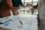 Three people standing around a table full of papers with data like bar graphs, pie charts, and more on them