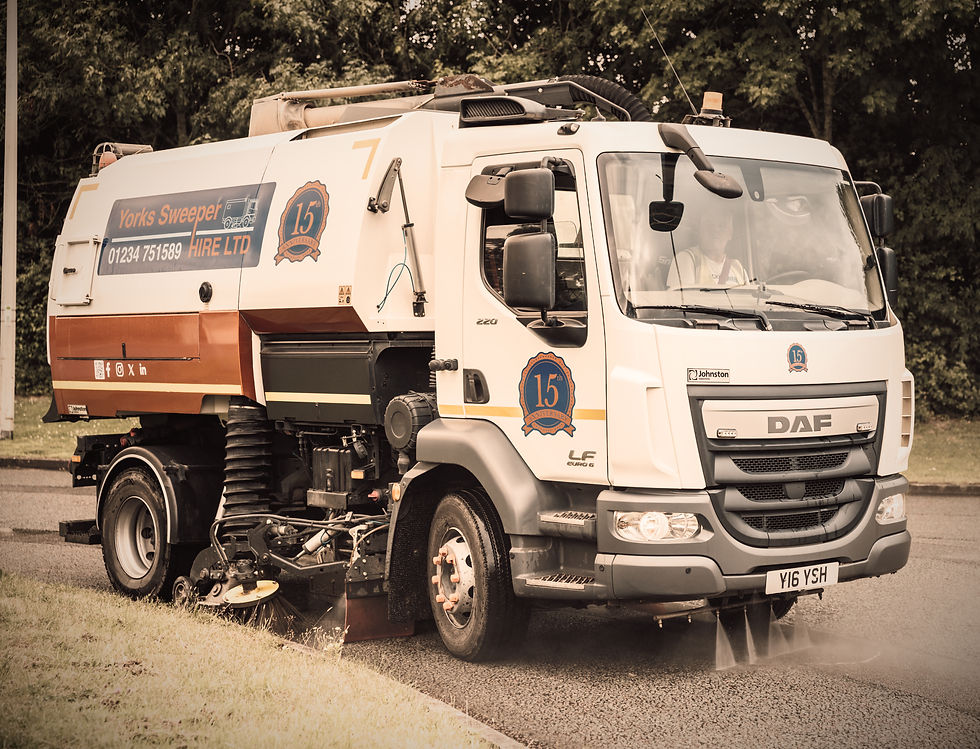 Street sweeper truck cleaning road with water jets, labeled "Yorks Sweeper Hire Ltd." Trees in background. Sepia tone. License: Y16 YSH.