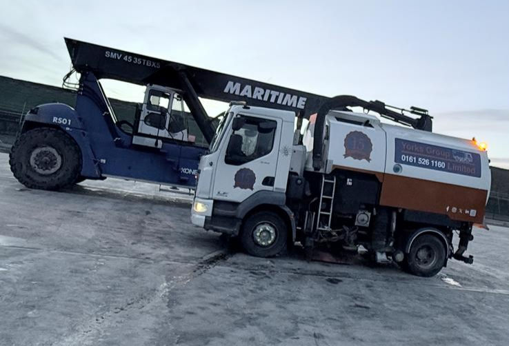 A blue forklift labeled "Maritime" lifts a street sweeper on a concrete surface. Overcast sky. Yorks Sweeper Hire sign and phone number visible.