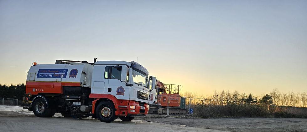 Road Sweeper Bedford. Street sweeper truck and excavator on dirt lot at sunset. Truck displays "Yorks Sweeper." Calm evening sky in background.