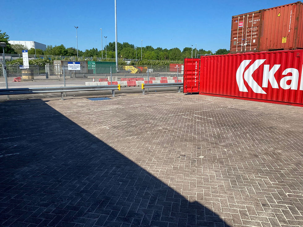 Red shipping containers on paved ground in a sunny industrial area, with fencing, trees, and clear blue sky in the background. Oil spill clean up