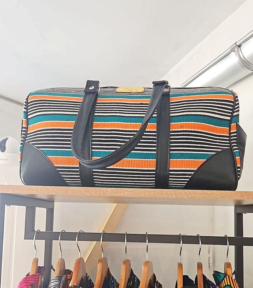 Sac de voyage en cuir noir et tissu africain rayé créé artisanalement par Nina Goha.