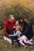 A family snuggles together in tall fall grasses while giggling.