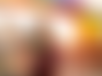 A gender-fluid person wearing a colorful shirt joyfully waves a rainbow flag in the air above their head.