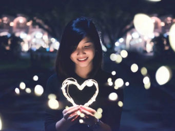 A person is standing in the foreground of the photo holding a heart made of string lights and smiling. They are surrounded by lights and their face is lit up.