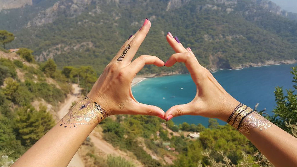 A pair of hands are coming together in the shape of a heart. The background is a beautiful sunny picture of green hills and blue water.