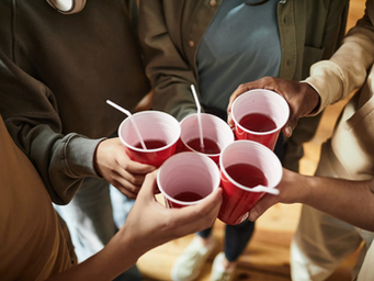 A group of young people are holding red plastic Solo cups filled with red liquid and straws at a party.