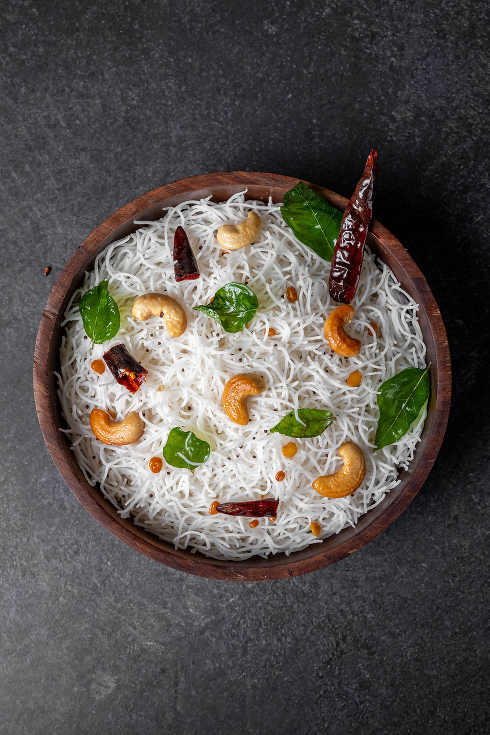 Concord Rice Sevai – traditional South Indian rice vermicelli garnished with curry leaves, cashews, and dried red chilies, served in a wooden bowl.