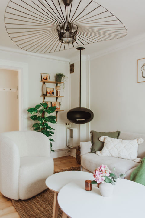 Cozy living room featuring buttery beige walls, boucle' textures, greenery and a ceiling hung fireplace