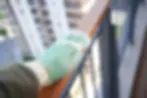 A hand of a person cleaning a balcony railing in a high-rise apartment