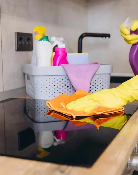 Professional cleaner wearing gloves wiping a kitchen stovetop with a microfiber cloth.webp