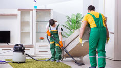 Two professional house cleaners vacuuming and dusting a bright living room in a Toronto home