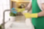 A person using a lemon as a cleaner in a spray bottle to wipe the faucet and sink