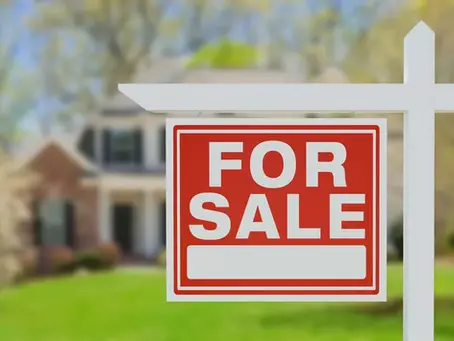 Real estate for sale sign on a green lawn in front of a house in spring