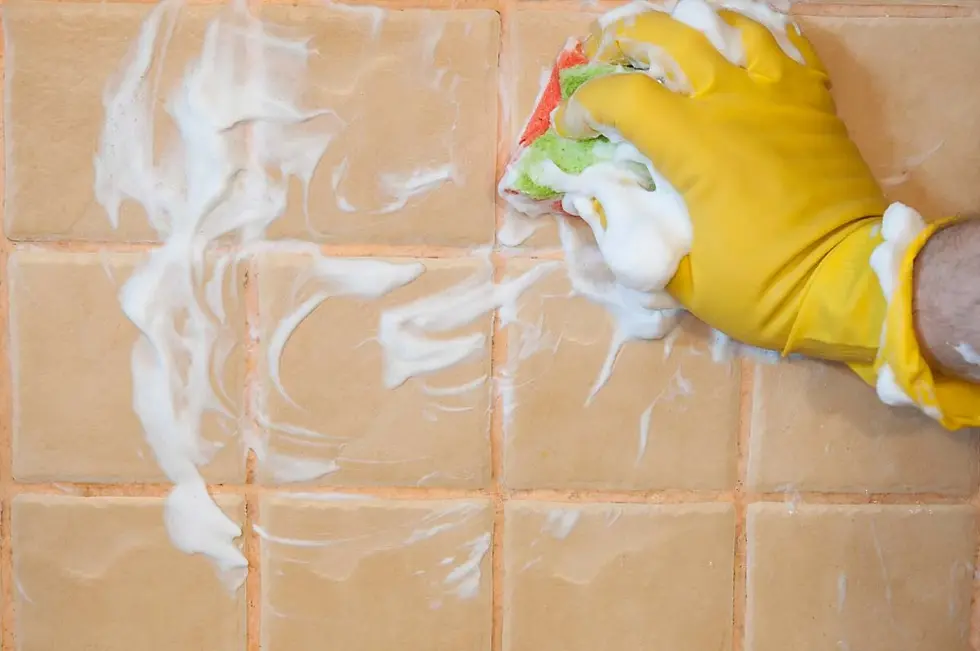 A gloved hand using a sponge to clean bathroom tiles and grout