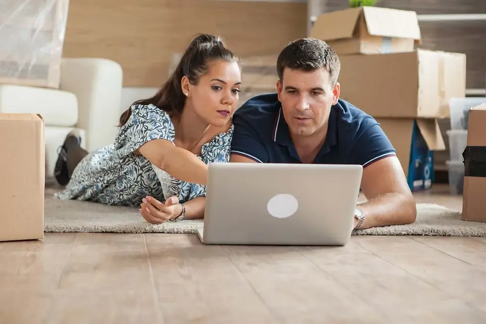A couple uses a laptop on the floor of their new home surrounded by moving boxes