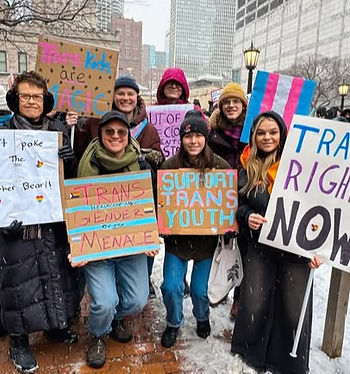 Seven protesters in the snow with homemade signs for trans rights including: "don't poke the mother bear," "Trans Gender Menace," "Support Trans Youth," "Trans Kids are MAGIC," and a trans flag.