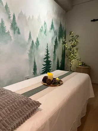Green nature-inspired massage room with a decorative light tree and misty forest wall art.
