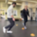 A physical therapist walks alongside a patient working on mobility with cones on the ground
