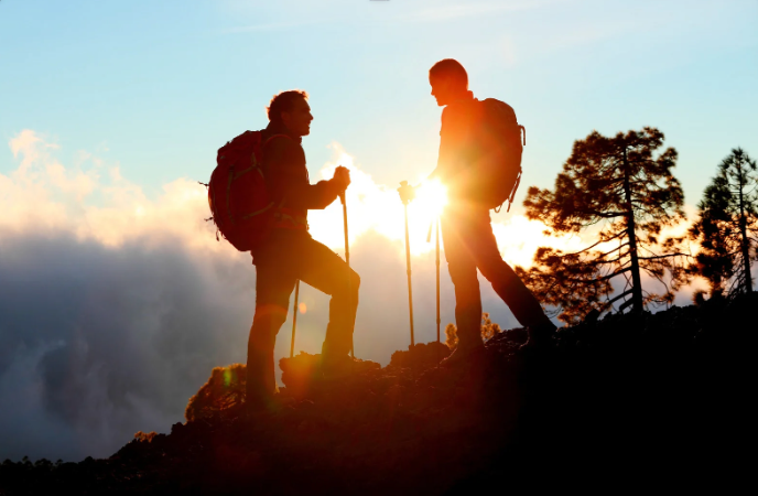 Hier stehen zwei Wanderer am Berg in Aktivität. Sie sprechen miteinander, während sie wandern.